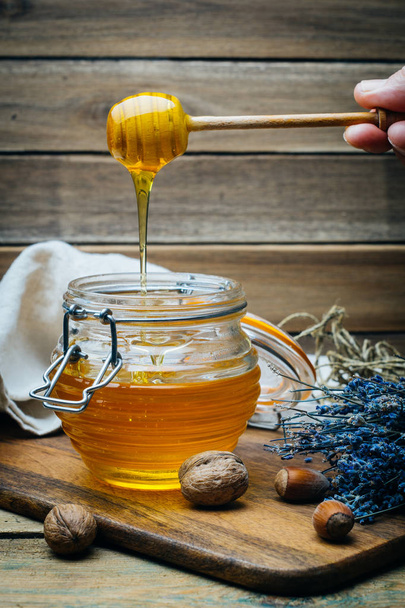 Miele in un barattolo con tuffatore di miele in legno su una tavola di legno con cracker, noci e fiori di lavanda
 - Foto, immagini