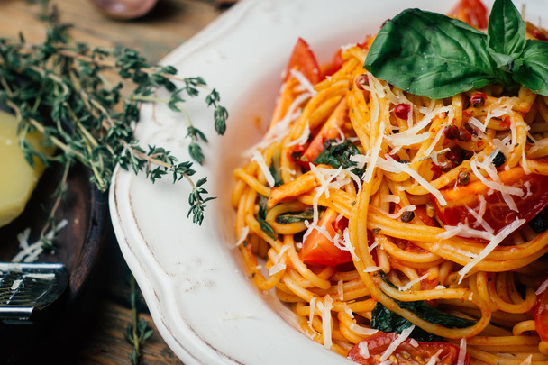 Špagety s rajčatovou omáčkou, parmezánem a bazalkou na bílé plotně. Klasické rajčatové špagety: Vegetariánská rajčatový bazalkové těstoviny. Staré dřevěné pozadí - Fotografie, Obrázek