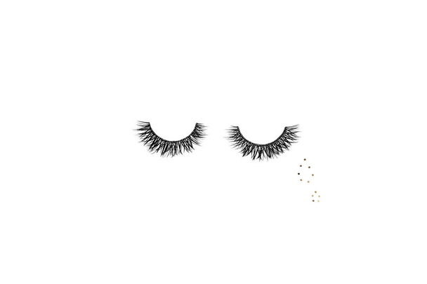 Dramatic black long false eyelashes placed in the shape of a human eye decorated with two teardrops of golden glitter isolated on white background shot with studio light - Photo, Image
