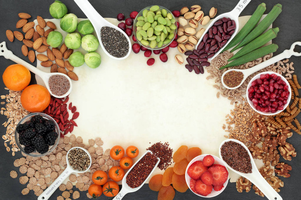 High fibre super food background border with fruit, vegetables, seeds, nuts, whole wheat pasta, cereals & grains. Foods with omega 3, anthocyanins, antioxidants & vitamins. On parchment paper & slate. - Photo, Image