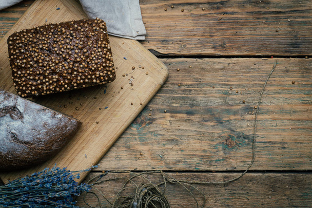 Baked homemade rye dark bread with coriander seeds and lavender on rustic wooden table background. Copy space. - Φωτογραφία, εικόνα
