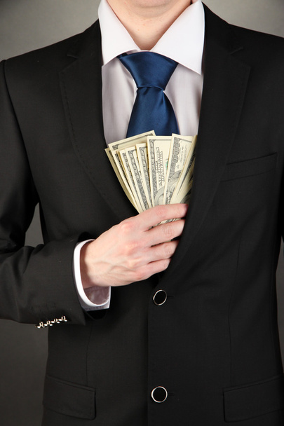 Business man hiding money in pocket on black background - Zdjęcie, obraz