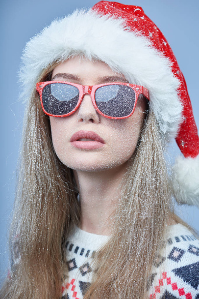 Frozen girl with snow on face wearing Santa hat and sunglasses - Fotoğraf, Görsel