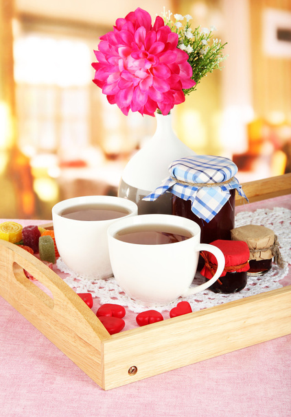 Cups of tea with flower and jam on wooden tray on table in cafe - 写真・画像