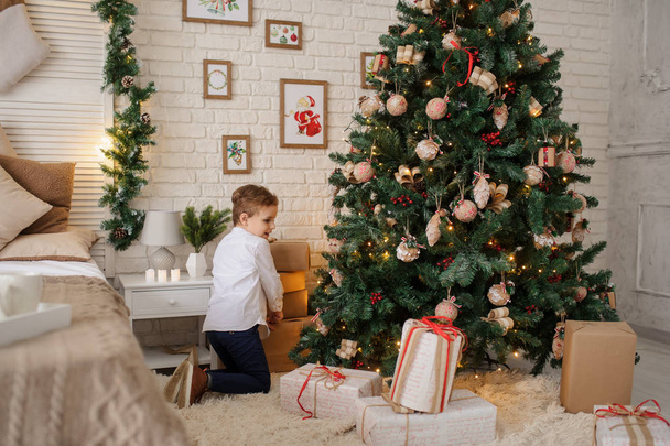クリスマスツリーとベッドの近くでプレゼントを手にした6歳のブロンドの男の子 - 写真・画像