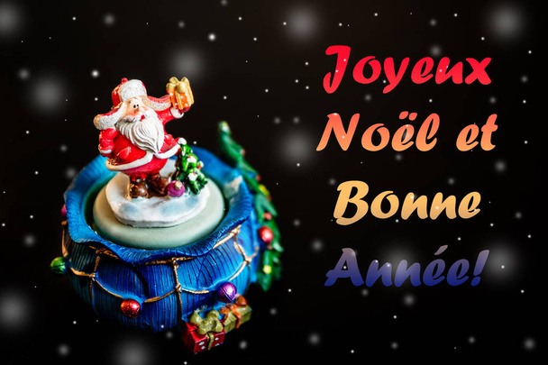 niedliches Spielzeug Weihnachtsmann isoliert auf schwarzem Hintergrund mit Schneeflocken und Farbbeschriftung joyeux noel et bonne annee in Französisch - Foto, Bild