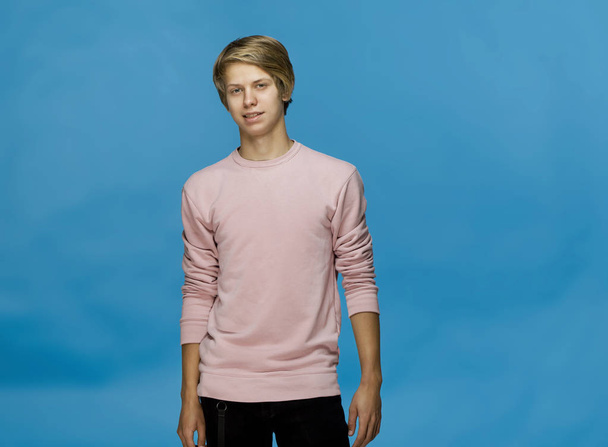 Handsome happy smiling young man wearing pink blouse studio portrait against blue wall - Foto, Bild