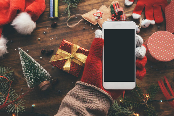 Smartphone in hand for Christmas season mock up with festive holiday decoration in background. - Foto, Imagem