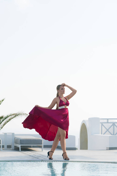 attractive girl in red dress posing near the pool. - Фото, изображение