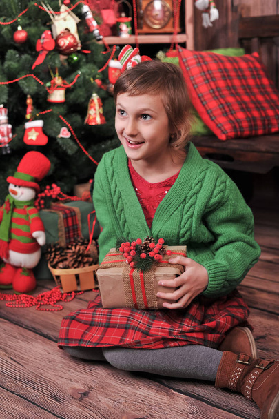 une fille en vêtements rouges et verts ouvre un cadeau de Nouvel An ou de Noël près du sapin de Noël
 - Photo, image