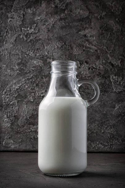 Healthy natural cow milk in glass bottle on dark gray concrete background - Фото, изображение