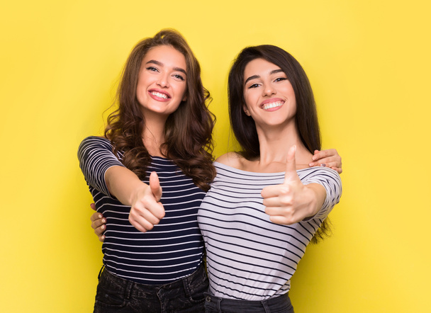 Cute women friends showing thumbs up on yellow background - Фото, изображение