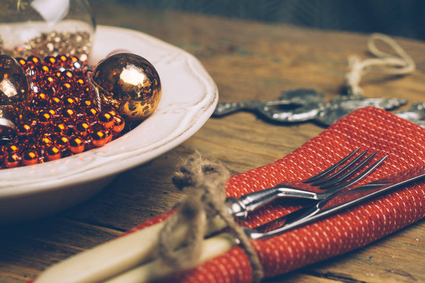 Vakantie kerst voedsel achtergrond concept. Kerst tafel met een witte plaat en kerstversiering. Set bestek mes en vork op een rode servet. Oude rustieke vintage hout achtergrond. Kopiëren van ruimte. - Foto, afbeelding