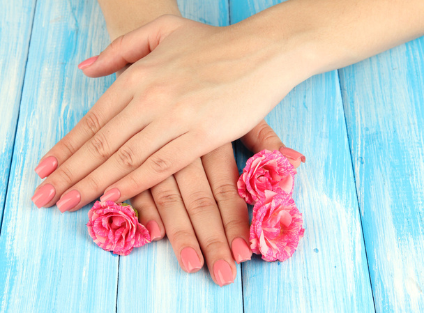 Woman hands with pink manicure and flowers, on color wooden background - Fotó, kép