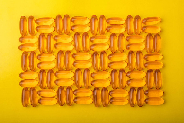 Omega 3 capsules from fish oil on a yellow background. Texture, pattern - Foto, Imagen