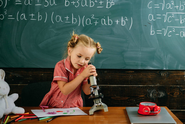 Little girl learn using microscope at school lesson. Cute child look in microscope optical instrument at science classroom. Where little things mean a lot - Foto, Imagem