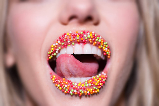 Sweet Lips. Female mouth decorated with candy. Compliments and sweet words. Beautiful mouth of a young girl with creative lipstick. Makeup for a Christmas party. Seductive tongue and white teeth smile - Photo, Image