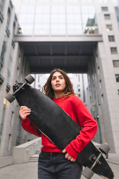 Ritratto di strada di una ragazza attraente in abbigliamento casual, in posa con un longboard nelle mani dello sfondo dell'architettura moderna. Street concept, ragazza con skate
 - Foto, immagini