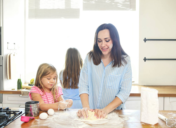 幸せな若い母と娘が台所で生地のふるいを通して小麦粉を注ぐ  - 写真・画像