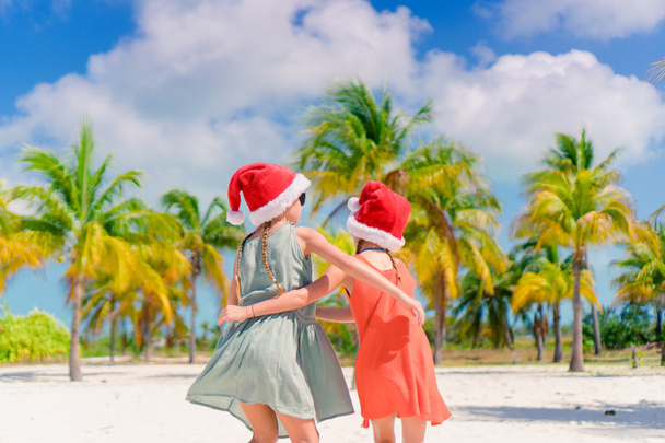 Αξιολάτρευτο κοριτσάκια σε καπέλα Santa κατά τη διάρκεια της διακοπές στην παραλία να διασκεδάσουμε όλοι μαζί - Φωτογραφία, εικόνα