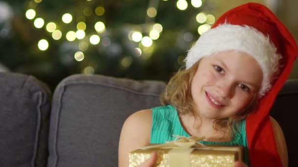 Happy child opening Christmas gift box. Funny baby dressed in Santa Claus hat in bedroom. Portrait of smiling kid at home. Xmas holiday concept - Filmagem, Vídeo