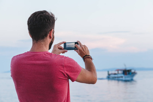 Молодой турист фотографируется со смартфоном у моря
 - Фото, изображение
