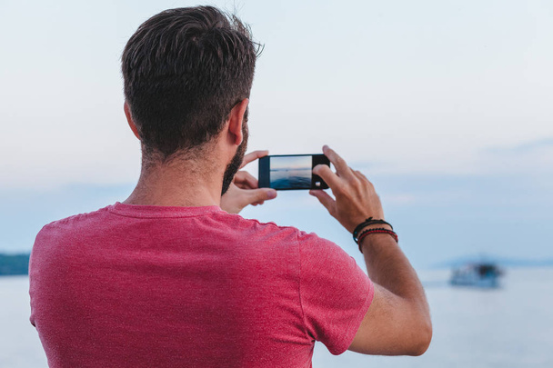 Jonge man toeristische nemen foto met smartphone door de zee - Foto, afbeelding