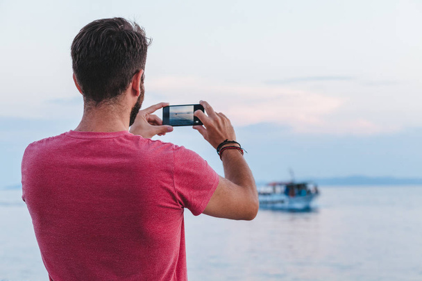 Young man tourist taking photo with smartphone by the sea - Foto, Bild