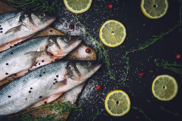 Friss nyers tengeri süllő hal, fűszerek, só, citrom és kakukkfű a fából készült konyhai deszkán főzés előtt. Tengeri sügér hal - Fotó, kép