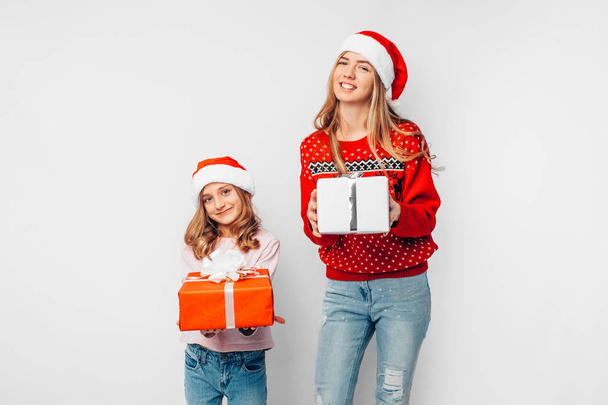 Mom and daughter celebrate the New Year, in Santa hats and Christmas sweaters, with gifts in their hands, on a white background. - Photo, image