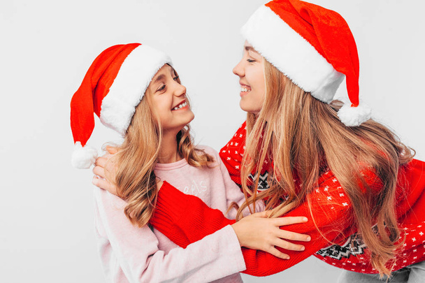 Мама і дочка носять капелюхи Санта-Клауса і в Різдвяний светри обнялися. На білому тлі. Концепція міцну сім'ю. - Фото, зображення