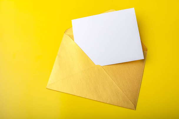 Mock-up carta o postal con un sobre de oro sobre un fondo amarillo. Copiar espacio
  - Foto, imagen