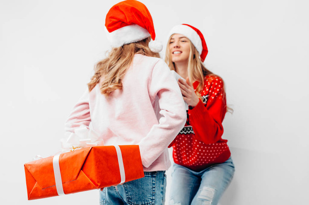 Mom and daughter celebrate the New Year, in Santa hats and Christmas sweaters, give each other Christmas presents, on a white background. - Foto, Imagen