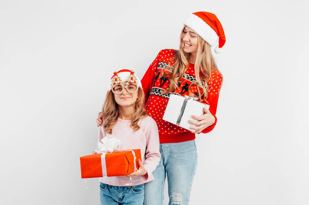 Mom and daughter celebrate the New Year, in Santa hats and Christmas sweaters, with gifts in their hands, on a white background. - Zdjęcie, obraz