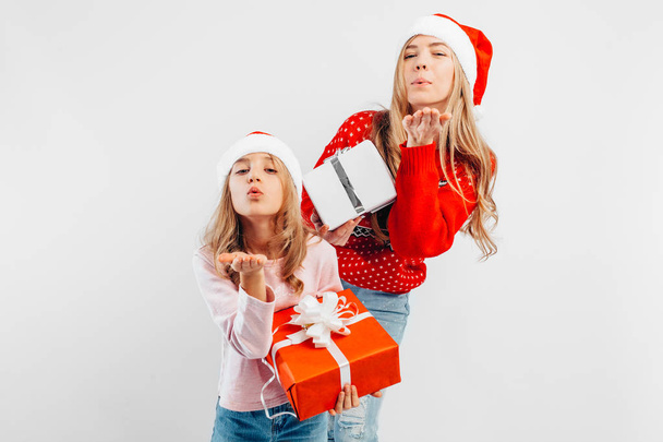 Happy mom and daughter celebrate New Year, in Santa hats and sweaters with gifts in their hands, on a white background. - Fotó, kép