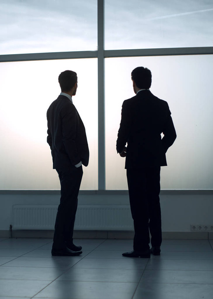 two businessmen look at the city from the window of the business center - Фото, изображение