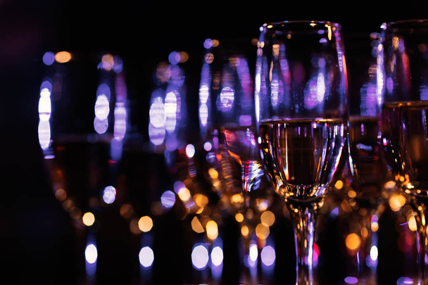 verres à champagne flous debout en plusieurs rangées dans une pièce sombre avec une lumière bleue
 - Photo, image