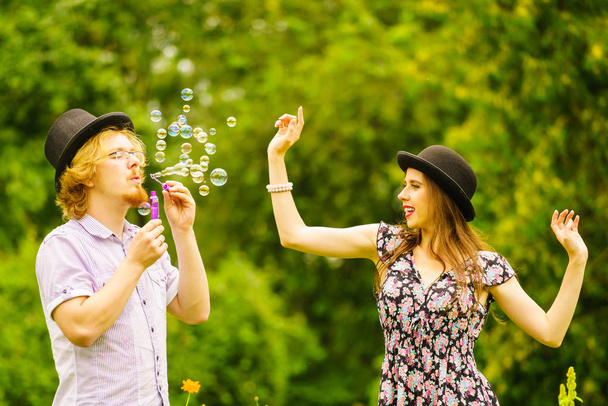 Happy funny hipster couple playing together blowing soap bubbles outdoor in spring park. - Fotó, kép