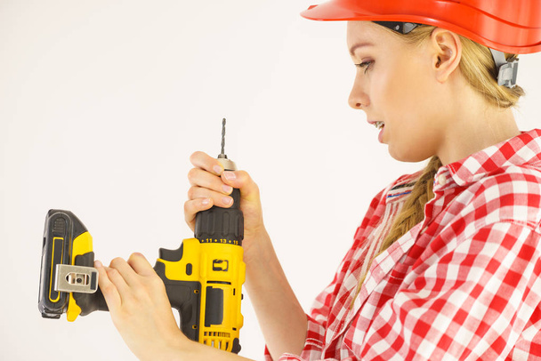 Woman wearing helmet using drill. Girl working at flat remodeling. Building, repair and renovation. - Photo, Image