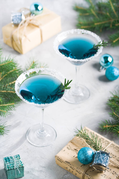 Christmas composition with martini drinks with rosemary and sugar decoration, fir-trees, balls, craft gift box in blue colors, gray concrete background. Winter holiday, New Year party concept. - 写真・画像