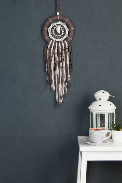 Beige brown dream catcher and white bedside table in bedroom decor on dark gray textured background. Copy space for text. - Photo, Image