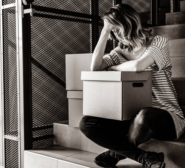 young woman with moving boxes sitting on stairs in house. . Image in black and white color style - Foto, afbeelding