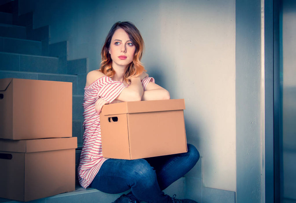 young redhead woman with moving boxes sitting on stairs in house. European ethnicity - Fotografie, Obrázek