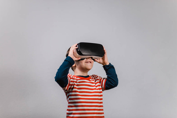 Heyecanlı çocuk Vr gözlük ile eğleniyor. Sanal gerçeklik kulaklık gri bir arka plana dayanır giyen çocuk portresi. - Fotoğraf, Görsel