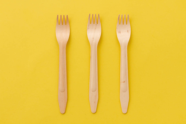 Three wooden forks on a yellow background. Plugs from natural materials. Safe disposable utensils to preserve the environment. - Fotoğraf, Görsel