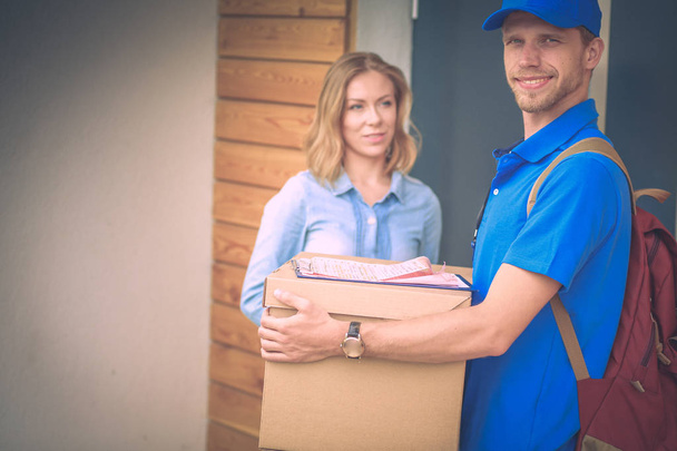 Smiling delivery man in blue uniform delivering parcel box to recipient - courier service concept. Smiling delivery man in blue uniform - Фото, зображення