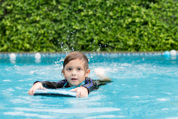 Little boy learning to swim in swimming pool, practicing with foam pad. - Photo, Image