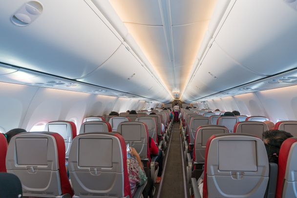 Intérieur de l'avion avec passagers sur les sièges et hôtesse de l'air en uniforme marchant dans l'allée
 - Photo, image