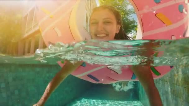 Mulher com óculos de sol em biquíni azul deitada em donut rosa inflável flutuar na piscina no dia ensolarado de verão. Olha para a câmara. Mulher biquíni piscina na melancia anel de borracha férias relaxantes
 - Filmagem, Vídeo
