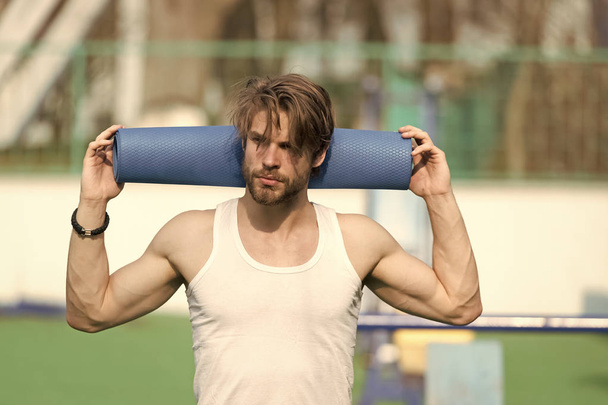 Man athlete with blue yoga mat in muscular hands - Foto, afbeelding